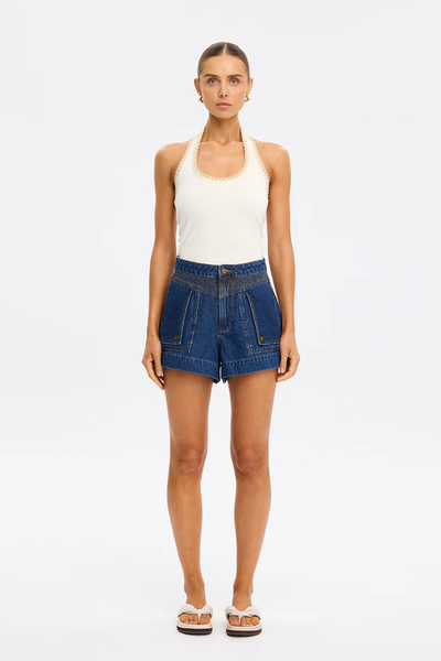 Full-length studio portrait of a model wearing the cream Kivari Rhea Halter Top, dark wash denim shorts, and cream slide sandals against a clean white background.