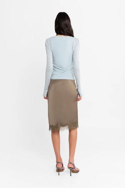Studio rear view of a model wearing the powder blue double-layer Kova top and a satin lace-trim midi skirt, highlighting the fitted silhouette.