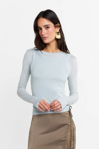 Close-up studio front portrait of a model wearing the double-scoop neckline Kova top in powder blue with gold statement earrings.