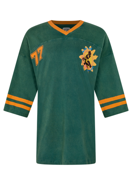 A clear flat-lay product image of the green tea dress isolated against a solid black background. This shot provides a clean, detailed view of the V-neckline, sleeve stripes, and graphic prints, emphasizing the vintage football jersey styling.