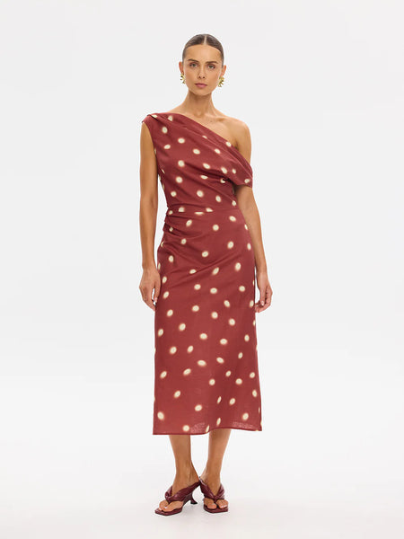 A full-length front-facing studio portrait of a model modeling the polka-dot asymmetric midi dress, styled with gold statement earrings and minimalist mule sandals.