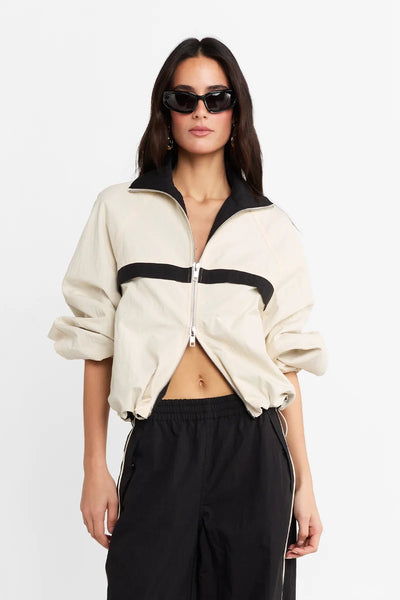 Waist-up studio portrait of a model wearing the cream and black spray jacket with sunglasses, posing against a white background.