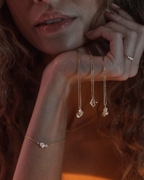 Editorial wrist view of the By Charlotte Quiet Radiance Bracelet in 18k gold vermeil styled alongside gold pendant necklaces and a matching gem ring.