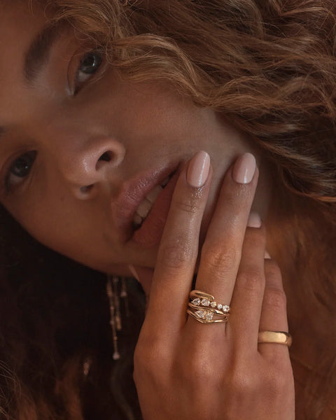 Close-up lifestyle view of a model's hand resting against her face, highlighting the stacked double-band design of the By Charlotte Celestial Path Ring in 18k gold vermeil.