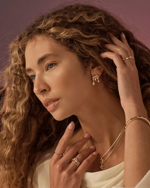 Model wearing the By Charlotte In the Stars Illusion Hoops styled with fine gold necklaces and rings in a warm editorial lifestyle portrait.