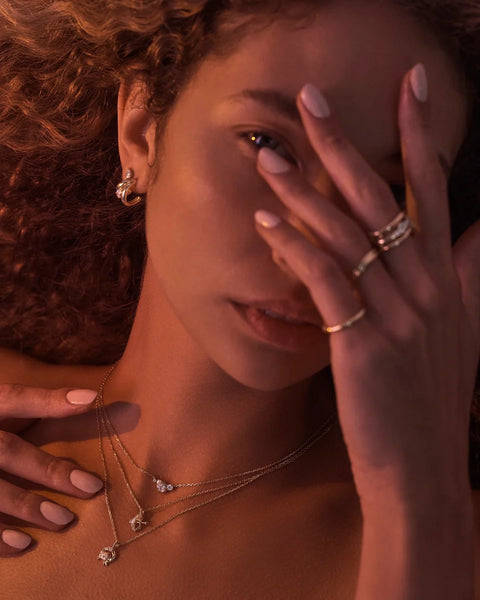 Editorial lifestyle campaign shot featuring a model styled in gold jewelry, highlighting the By Charlotte Celestial Path Hoops under warm ambient lighting.