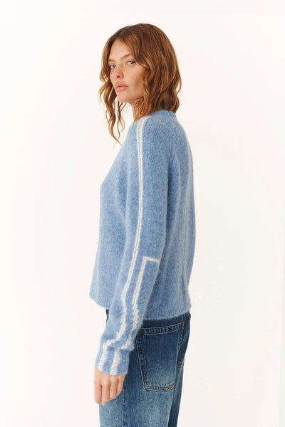Side profile of the Lana jumper illustrating the relaxed proportions and the visual interest of the sleeve stripes against the minimal sky-blue body.