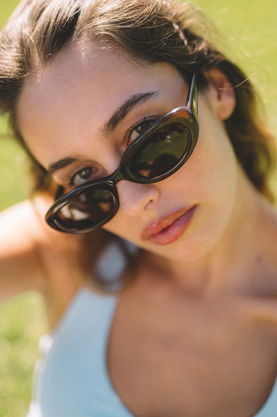 Close-up outdoor portrait of a dark-haired model wearing the Sito Shades Lourdes oval sunglasses in translucent milky coco brown acetate.
