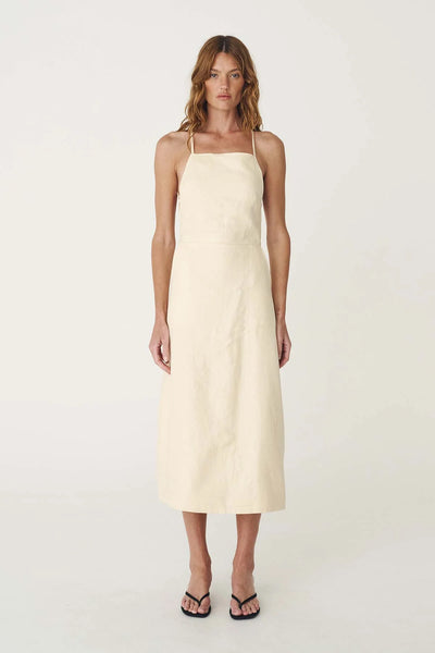 Studio front full-length view of a model wearing the butter creme apron-style linen midi dress.