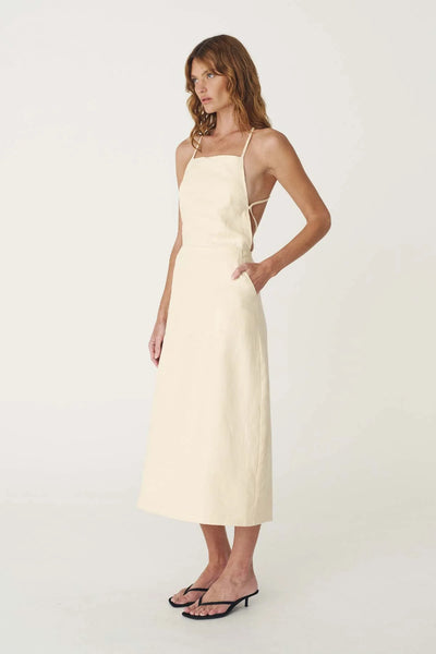 Studio side profile of a model wearing the butter creme linen midi dress paired with minimalist black sandals.