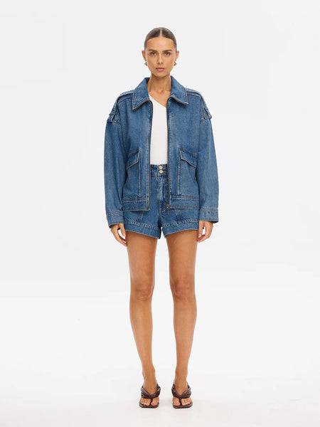 A three-quarter campaign shot highlighting the texture and utility details of the oversized Rita Denim Jacket zipped halfway up, styled as a coordinating set with matching denim.