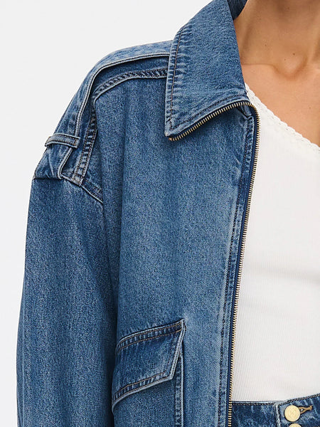 A macro detail shot of the denim jacket’s upper construction, focusing on the crisp contrast topstitching along the shoulder paneling, the full-length sleeve cuff detail, and the pointed collar.