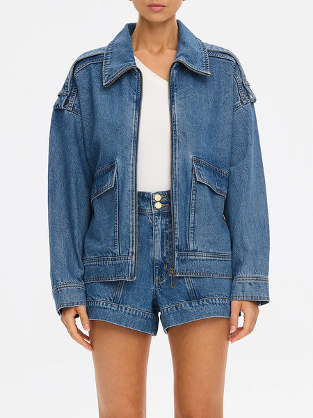 A clean studio portrait of a model standing straight-on in a coordinating denim set, showcasing how the oversized jacket pairs seamlessly with matching high-rise utility shorts.
