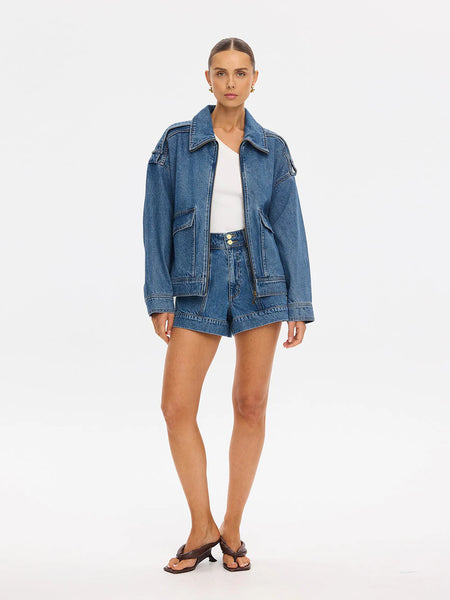 Full-length studio shot featuring a model posing from a three-quarter angle, highlighting the relaxed, slouchy silhouette of the vintage blue denim jacket paired with brown strappy kitten heel sandals.