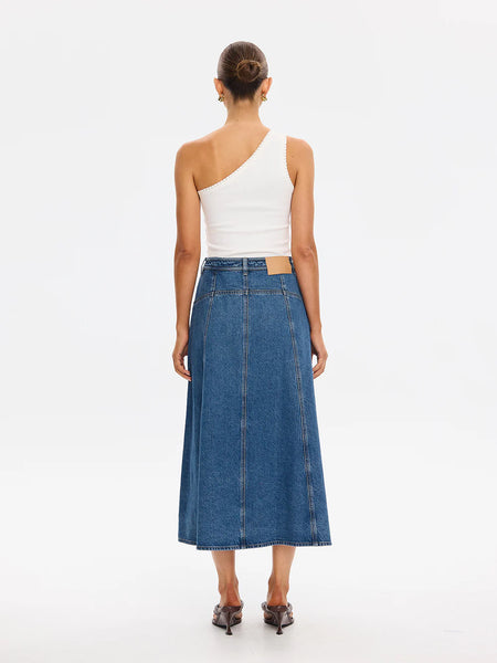 Full-length studio back view of a model showcasing the crisp center back yoke line, vertical panel detailing, and a classic tan leather logo patch on the waistband of the A-line denim midi skirt.