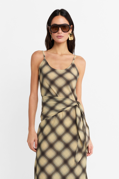 Close-up front view of a model wearing the check maxi dress, highlighting the scoop neckline, wrap-around waist tie detail, and statement sunglasses.