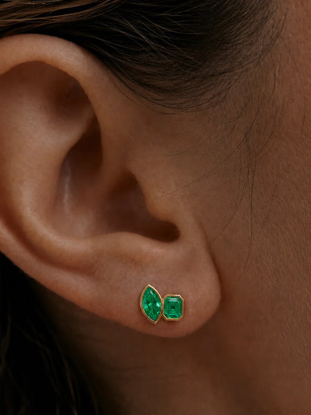 Macro close-up of a model's earlobe displaying the emerald-cut and marquise-cut green CZ stones in a gold bezel setting.