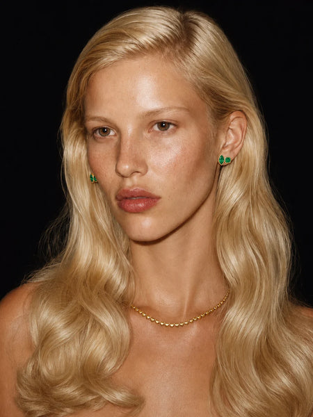 Front-facing portrait of a model wearing the emerald and gold stud earrings, showcasing the bold green cubic zirconia stones against her blonde hair.