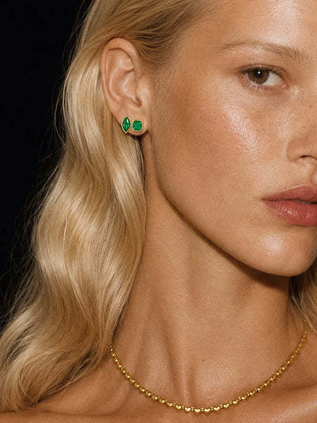 Close-up profile portrait of a model wearing the Avant Studio Marguerite Stud Earrings in Emerald with gold plating, paired with a matching gold heart choker necklace.