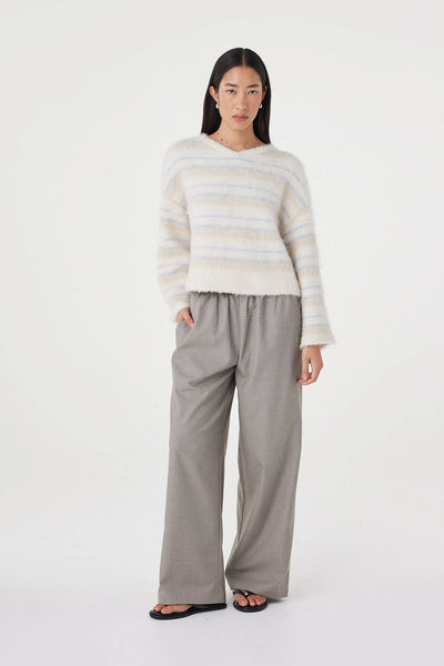 A relaxed studio pose with the model angled to the left, one hand casually resting in her pocket. This composition highlights the effortless layering potential of the fluffy knit, illustrating how the soft silhouette matches seamlessly with relaxed casual tailoring.