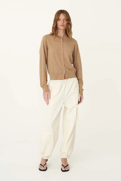 Full-length studio portrait of a model wearing the ROWIE Maeve Merino Spring Cardigan in Fawn Marle buttoned up, paired with relaxed off-white cargo pants and black thong sandals.