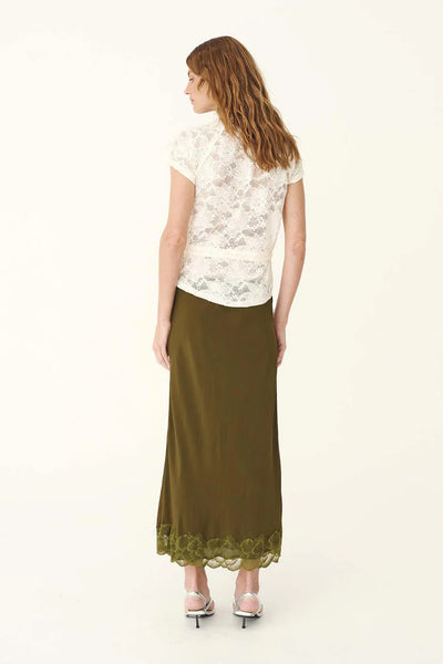 Rear view studio shot of a model wearing the ROWIE Marina Silk Midi Skirt in Olive paired with a short-sleeve lace blouse, showcasing the fluid bias-cut drape and tonal scalloped lace trim along the hemline.