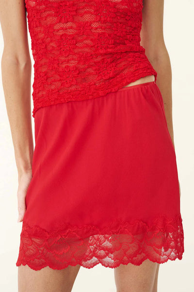 Close-up studio view of the ROWIE Marina Silk Mini Skirt in Flame Red, showing the fine elasticated waistband, fluid 100% silk crepe fabric, and scalloped floral lace hemline.