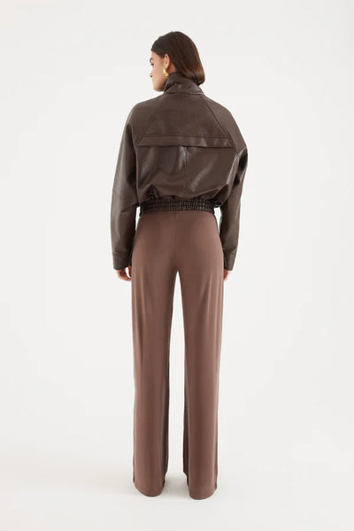 A full-length side profile studio image of the model standing against a white backdrop. The framing isolates the left profile of the outerwear garment, highlighting the exaggerated volume of the raglan sleeves, the extended funnel neck construction, and the tailored length from the highest point to the hem measuring 63cm.