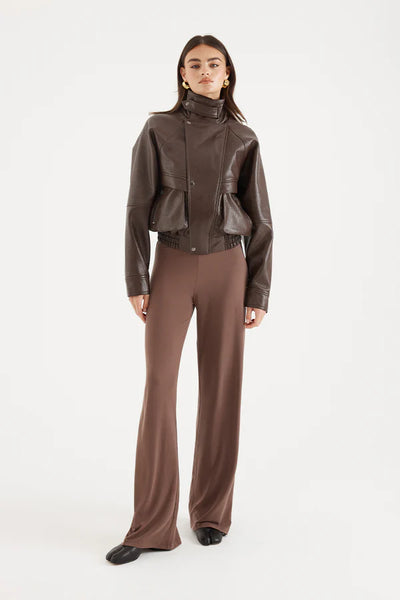A full-length front-on portrait of the model against a crisp white studio background, showcasing the jacket styled completely open and unzipped. This configuration reveals a coordinated midriff-baring brown top underneath, detailing the loose drape of the asymmetric lapels, the concealed zip closure interior structure, and the boxy streetwear tailoring through the chest.