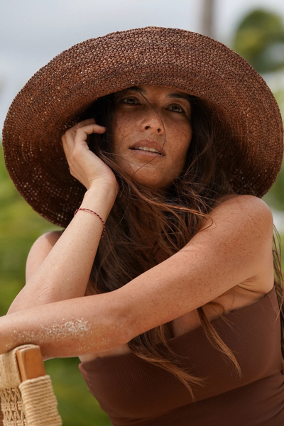 Close-up portrait of a model outdoors resting her hand near her face while wearing the cocoa raffia bucket hat.