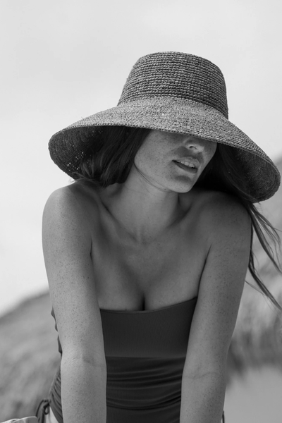 Black-and-white close-up portrait focusing on the front brim and texture of the cocoa raffia bucket hat.