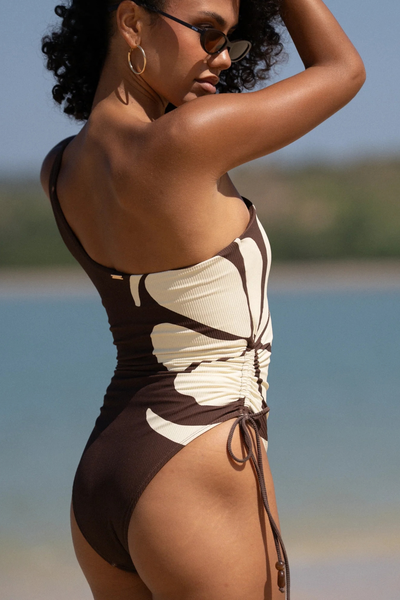 Close-up side profile view highlighting the one-shoulder neckline and side ruching of the swimsuit.