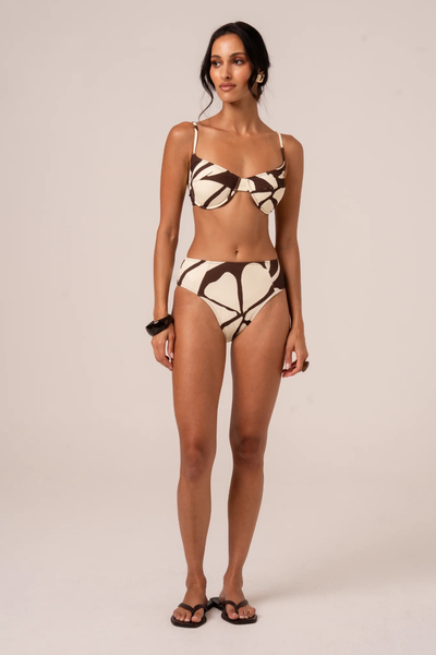 A full-length front studio shot of a model wearing the Ochre Lane Splice Mid Rise Bottom in the Ibisco print, highlighting the structured mid-to-high rise waist alignment and elongated high-cut leg lines.