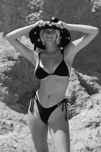 A three-quarter side angle studio portrait displaying the timeless monochrome black and cream polka dot motif, complementing a neutral resort wear aesthetic.