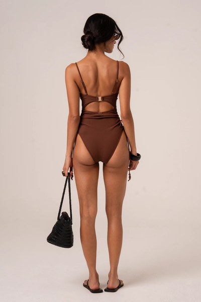 A side profile studio shot on a model, showcasing the adjustable side-tie gathers along the hip that allow for customizable leg height and leg-line elongation.