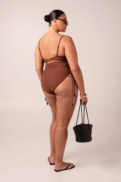 Studio rear three-quarter view of plus-size model Caitlin showcasing the open back, clasp detail, and medium coverage bottom of the chocolate brown swimsuit.