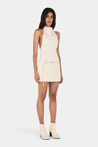 Three-quarter studio view of model wearing the Ownley Sammie Mini Dress in Cream, showing the high cowl halter neck and side waist belt extension.