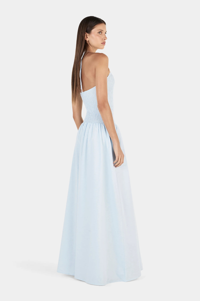 Studio rear three-quarter view of a model wearing a cornflower blue halter neck maxi dress, highlighting the open back and thin shoulder straps.