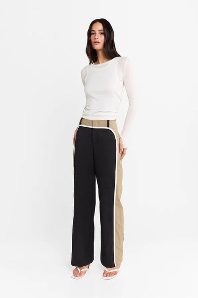 Studio front full-length view of a model wearing the white stretch-fabrication Kova top paired with wide-leg trousers and heeled sandals.