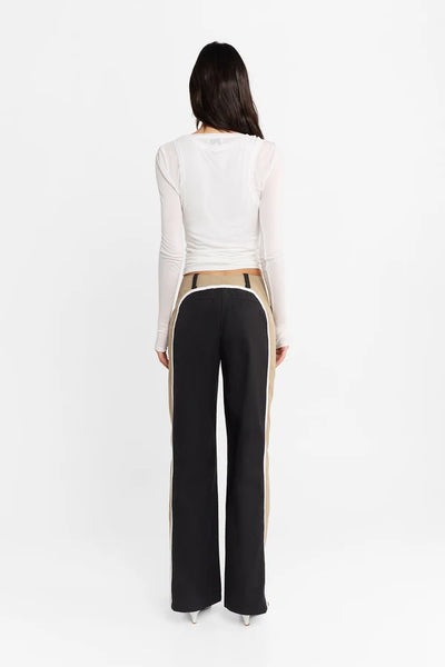 Studio rear view of a model wearing the white double-layer Kova top and contrast-paneled trousers, showcasing the fitted silhouette.