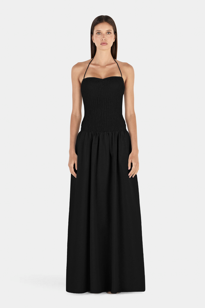 Full-length studio front view of a model wearing a black halter-neck maxi dress featuring a sweetheart-contoured smocked bodice and a flowing maxi-length skirt.