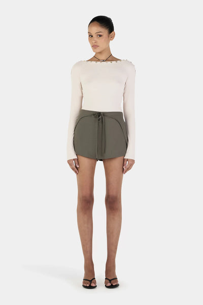 A full-length front studio shot showcasing the cream fitted top paired with contrast forest green shorts, emphasizing the sleek 50cm center front body length.