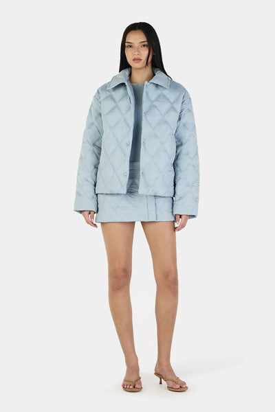 A full-length front studio shot of a model wearing the Ownley Quinton Quilted Jacket in Ice Blue, showcasing the oversized boxy silhouette, geometric quilted pattern, and clean front press snap closures.