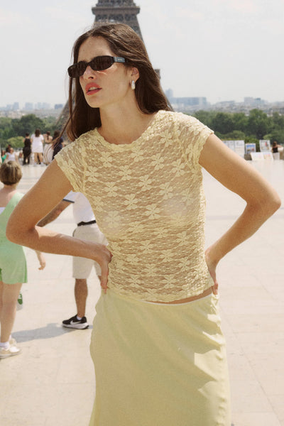 Outdoor editorial shot of a model wearing sunglasses, the semi-sheer creme lace top, and a matching skirt with the Eiffel Tower in the distance.