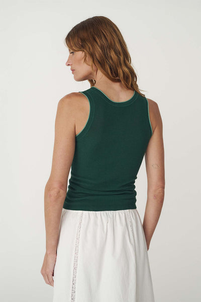 Rear studio view of a model wearing the bottle green contrast-trim tank top tucked into a white tiered skirt.
