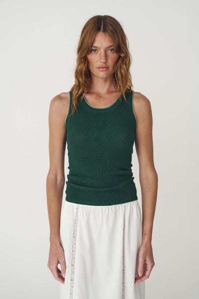 Front studio view of a model wearing the full-length bottle green ribbed tank top with contrast trim paired with a white skirt.