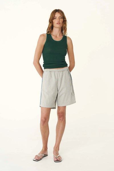 Full-length studio view of a model wearing the bottle green ribbed knit tank paired with patterned plaid shorts and thong sandals.