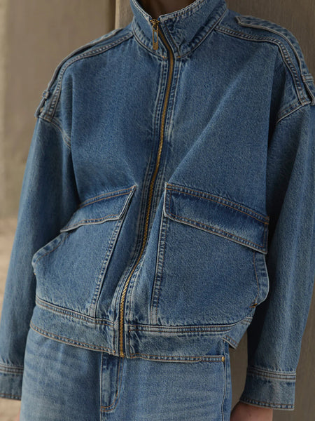 A three-quarter campaign shot highlighting the texture and utility details of the oversized Rita Denim Jacket zipped halfway up, styled as a coordinating set with matching denim.