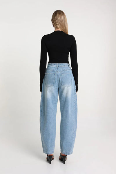 A full-length front studio shot of a model presenting the black stretch fabrication long-sleeve tee, showcasing its high scooped neck and sleek, body-hugging fit styled with loose-fitting blue denim.