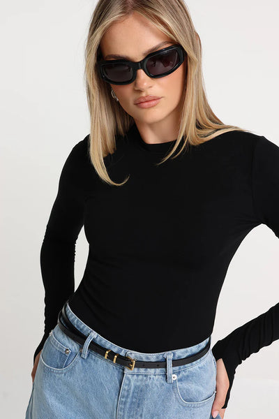A close-up studio shot of a model wearing the black fitted baby tee, accessorized with black rectangular sunglasses and a thin black leather belt with gold hardware on her jeans.